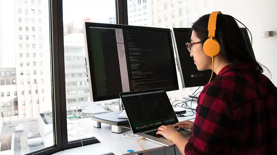 Software developer working on her multi-display PC, software code is displayed on the screens.